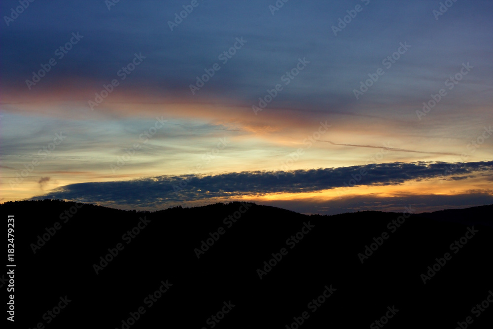 Landscape with forest and silhouettes of trees at sunset between clouds