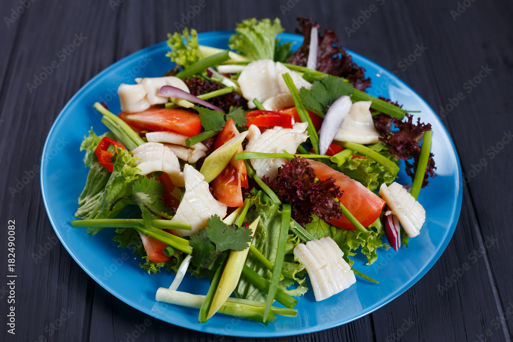 Delicious fresh salad with squid on black kitchen background, close up. Pan-Asian, oriental cuisine, tasty appetizing seafood Delicious fresh salad with squid on black kitchen background, close up. Pan-Asian, oriental cuisine, tasty appetizing seafood