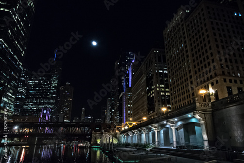 Chicago city riverwalk promenade at night with vintage drawbridge  illuminated urban downtown buildings and the moon.