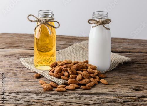 Peeled almonds with bowl and Bottle of almond milk and oil on rustic wooden