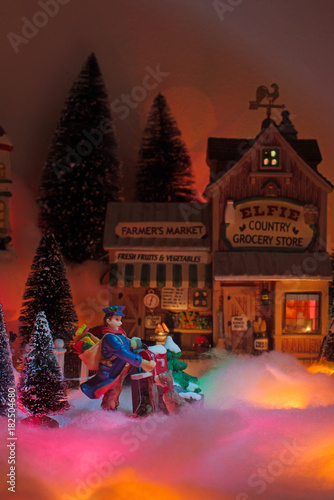 postman delivers holiday message with the backdropl is a snow Christmas town with elfie grocery store facade