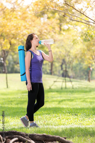 Young girl with a yoga mat and a bottle of water in the park