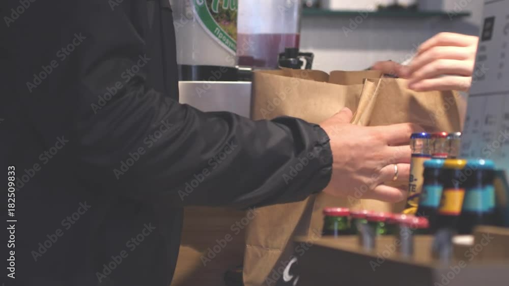 Hands putting burgers into bag. Man buys packaged food in cafe