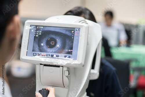 Woman looking at refractometer eye test machine in ophthalmology photo
