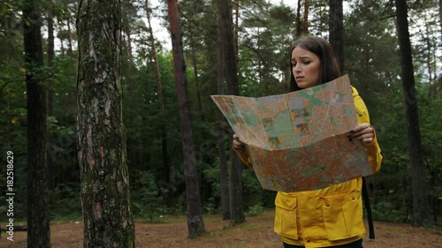 Young beautiful woman in yellow coat getting lost in the forest. She looking for the route with a help of a map. Outside