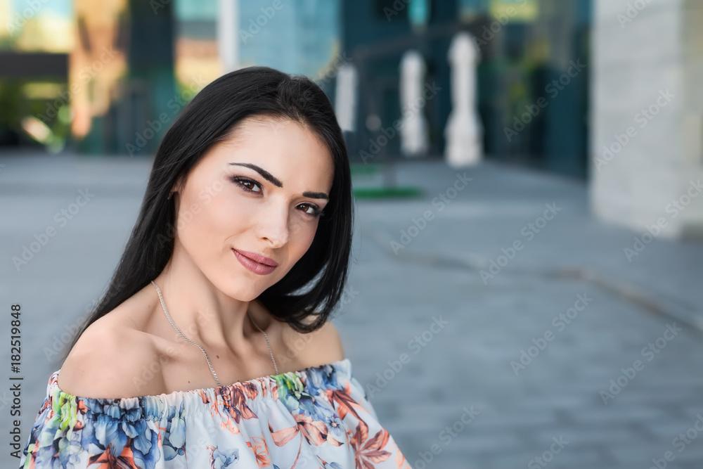 Young nice beautiful brunette teen with long hair in the street wearing white dress with flower pattern. Close up portrait