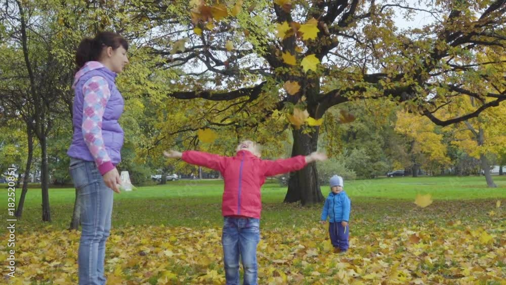 Happy family throws yellow leaves falling up. Mother with little son and daughter throwing leaves in Autumn in slow motion, smiling. Children playing in the autumn park foliage. Happy family throws yellow leaves falling up. Mother with little son and daughter throwing leaves in Autumn in slow motion, smiling. Children playing in the autumn park foliage.