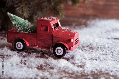 Red car carrying a Christmas fir tree on the snow background. Concept for Xmas times and Winter holidays. Copy space.