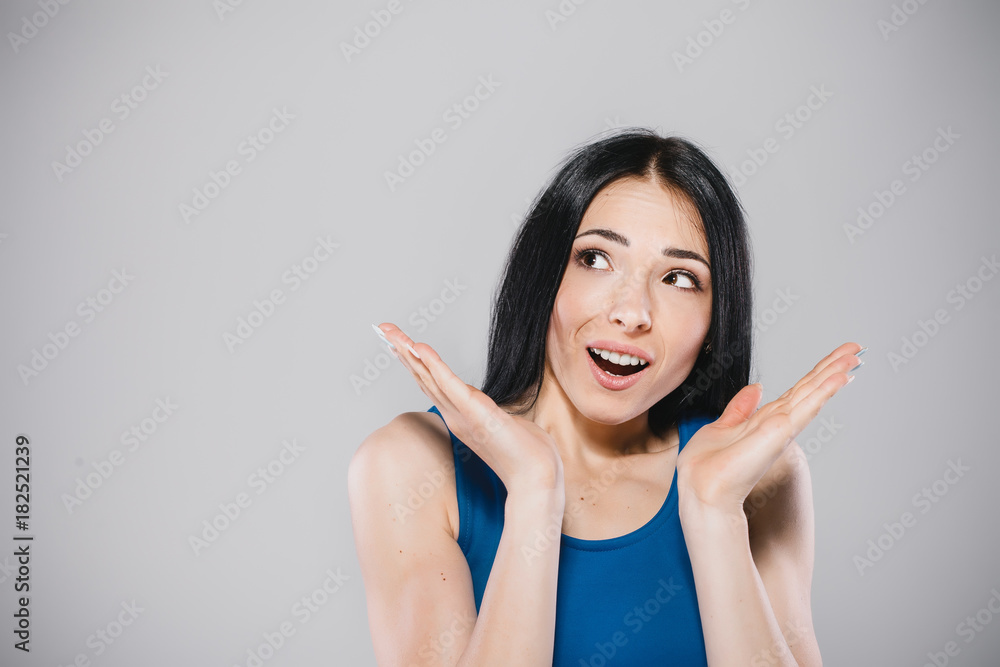 young woman with long brunette hair in blue dress surprised in photostudio on gray background young woman with long brunette hair in blue dress surprised in photostudio on gray background