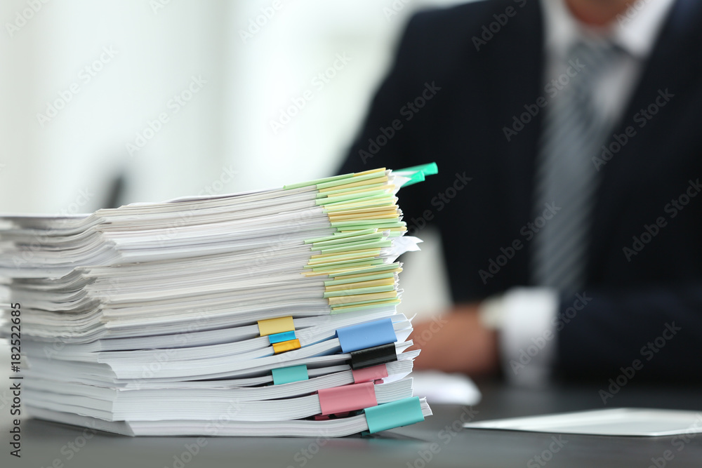 Stack of documents on table and blurred man in office Stack of documents on table and blurred man in office