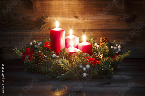 Fourth Advent - Decorated Advent wreath with four red burning candles on a wooden background with festive atmosphere