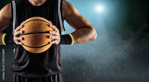 Basketball ball in a male hands, player in black with orange spo