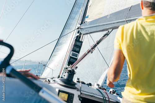 Professional sailor or yachtsowner controls sailboat with mainsail and spinnaker up, by observing data and information from devices on mast, wind speed and power
