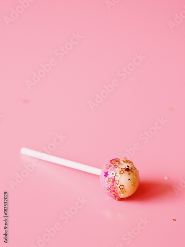 Close up lollipop with golden glitter on pink background.