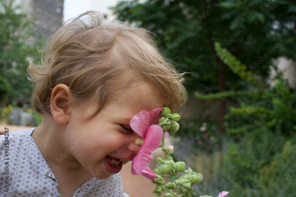 Beautiful laughing child and hollyhock flower in summer garden Beautiful laughing child and hollyhock flower in summer garden