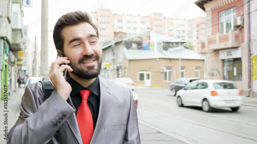 Young businessman in formal suit walking on the street and talking on the phone. Business and communication Young businessman in formal suit walking on the street and talking on the phone. Business and communication