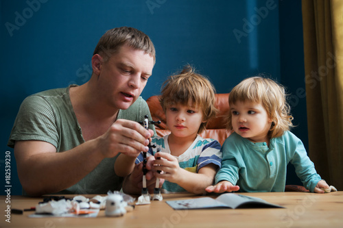 Family and childhood concept. Father and his little children play together plastic blocks and makes robot. 