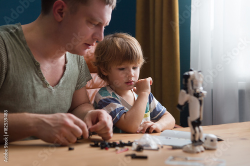 Family and childhood concept. Father and his little son play together plastic blocks and makes robot. 