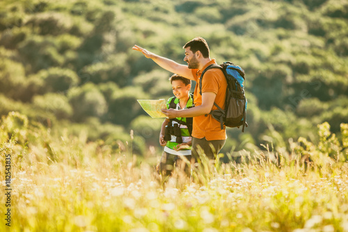 Father and son are hiking in nature in summer. They are looking at map. 
