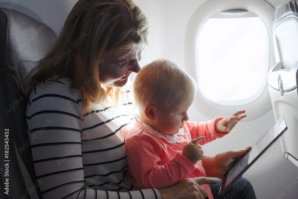 Fototapeta premium Mom and child playing tablet while flying on plane