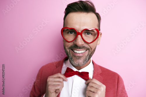Cheerful man with heart shape eyeglasses adjusting a bow tie