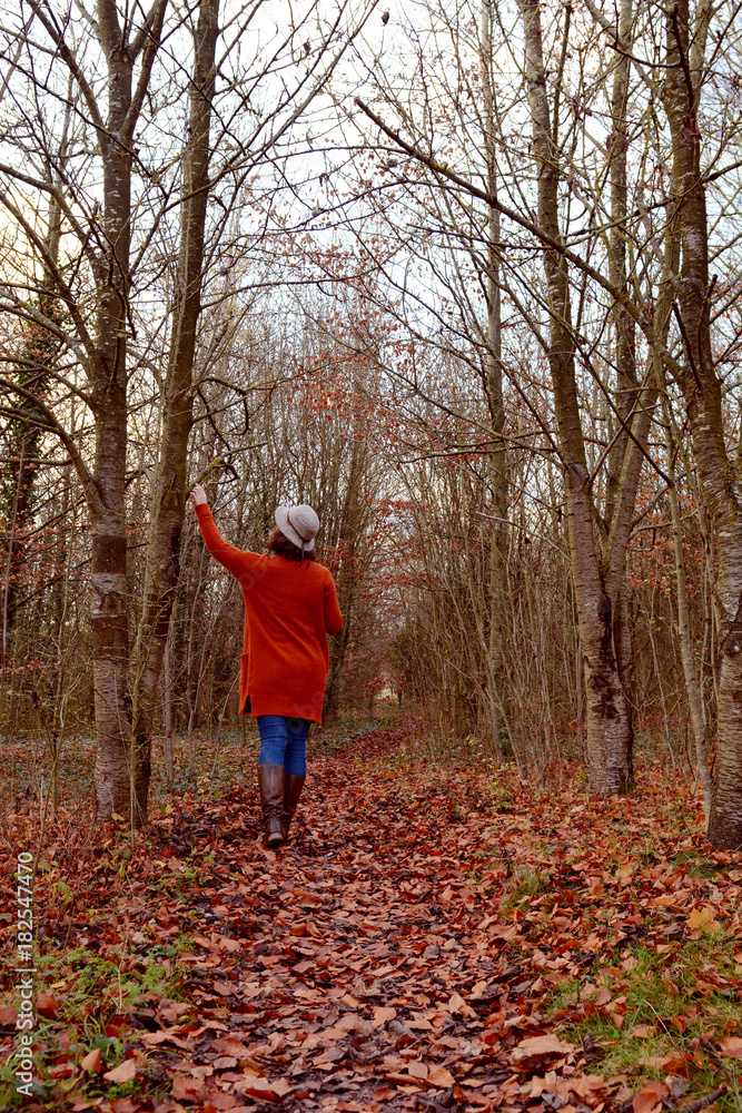 Woman walking down woodland path alone, touching trees Woman walking down woodland path alone, touching trees