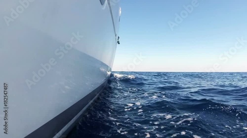 Luxury catamaran sailing through sea waves at bright sunny day. Side view from right hull close to water. Aegean sea, Greece.