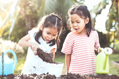 Two children asian little girl having fun to prepare soil for planting seedling young tree together in vintage color tone photo