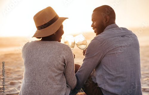 Картината върху платно Young African couple drinking wine and watching a beach sunset