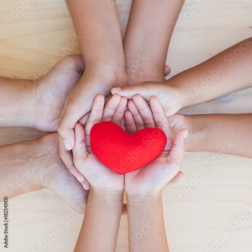 Red heart in parent and children holding hands together on wooden background. Family and friend stack hands with red heart showing unity, teamwork and love