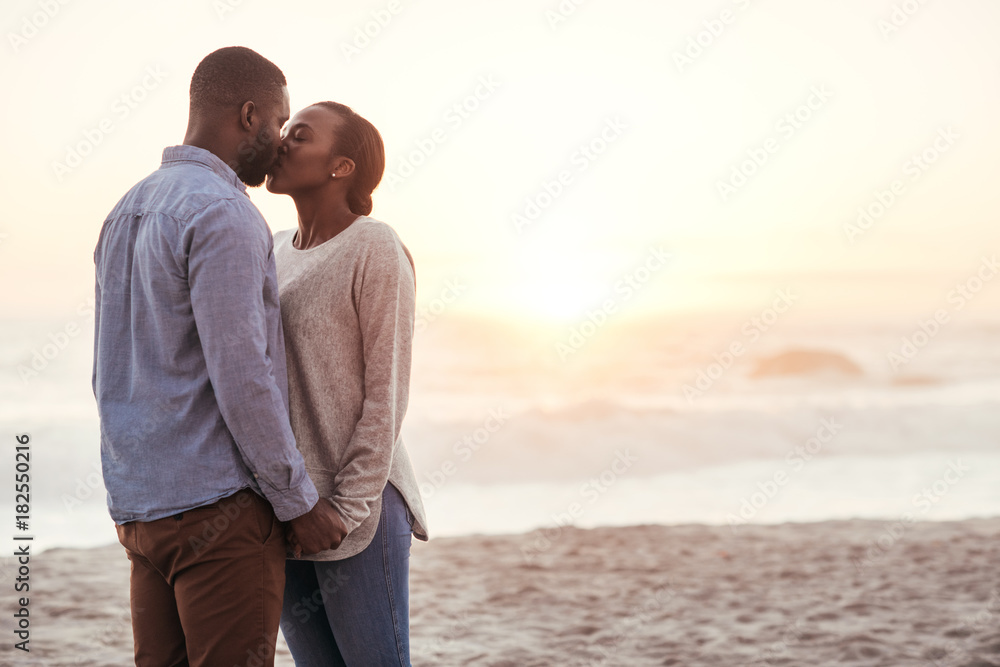 Romantic young African couple kissing on a beach at sunset
