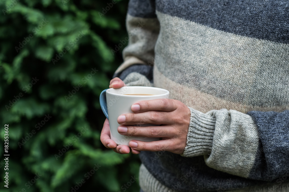 Hands holding a cup of warm coffee in a forest Hands holding a cup of warm coffee in a forest