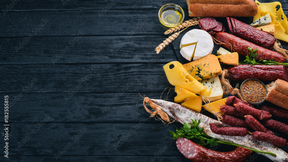 Assortment of cheeses and traditional sausages on a wooden background. Brie cheese, blue cheese, gorgonzola, fuete, salami. Free space for text. Top view.