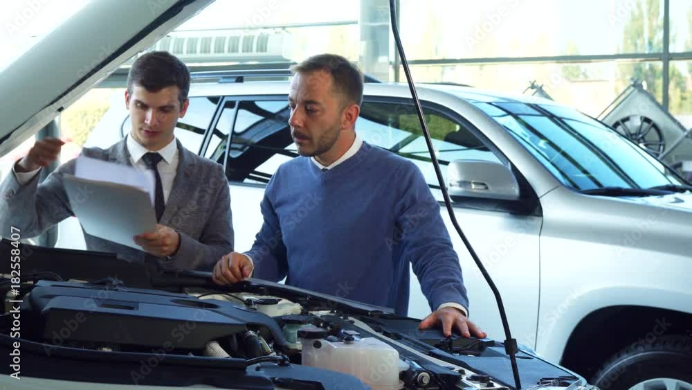 An attentive buyer and seller are studying the details in the open hood of the car An attentive buyer and seller are studying the details in the open hood of the car