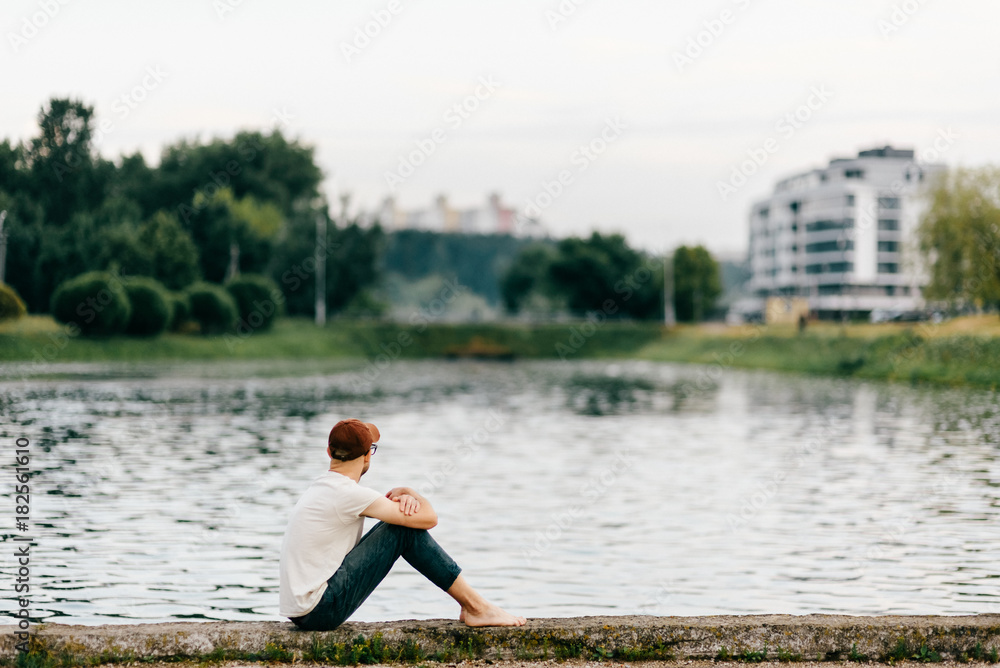 Barefoot lonely unknown adult man sitting on edge of embankment outdoor. Homeless poor person in depression. Waiting for help. Problematic life. Psychological dramatic male portrait. Friendless person