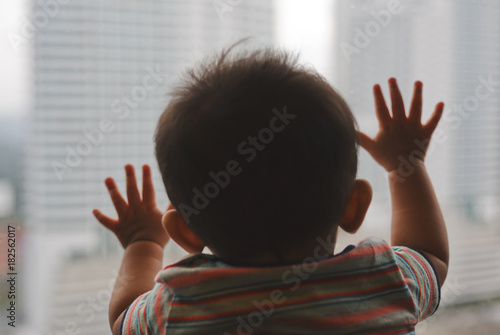 A baby boy looking through window of an apartment.