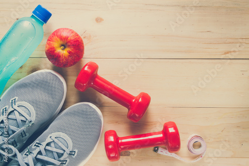 Fitness equipment consisting of dumbbells, training shoes and Electrolyte Drink on wooden texture and background, vitamin from apple
