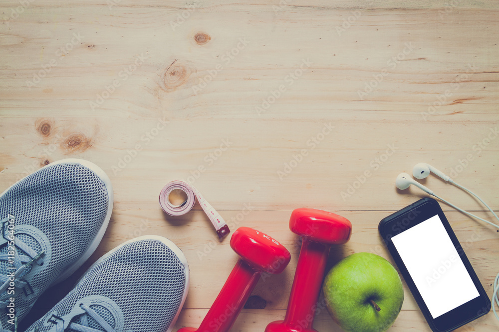 Fitness equipment consisting of dumbbells, training shoes and Electrolyte Drink on wooden texture and background, vitamin from apple, smartphone for listening to music Fitness equipment consisting of dumbbells, training shoes and Electrolyte Drink on wooden texture and background, vitamin from apple, smartphone for listening to music