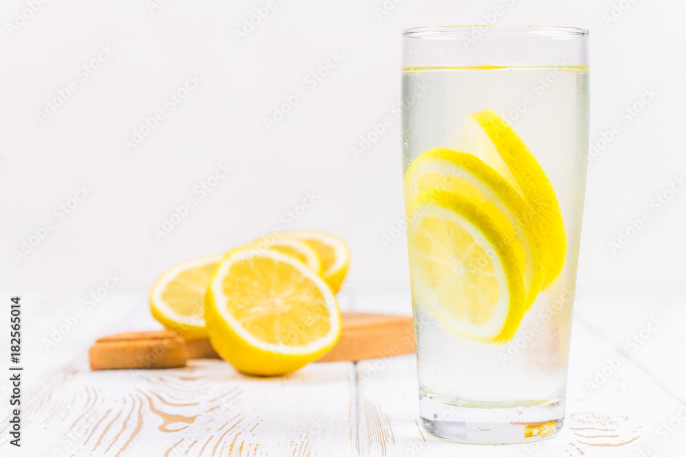 A glass beaker and a jug of cold lemonade on a white wooden background surrounded by lemons. A glass beaker and a jug of cold lemonade on a white wooden background surrounded by lemons.