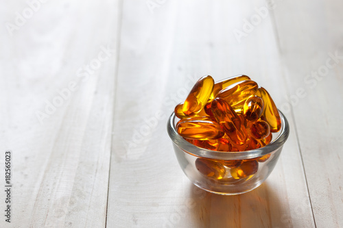 Fish oil capsules on wooden background and texture, vitamin D supplement, selective focus