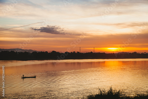 Fisherman floats on a lake at sunrise.