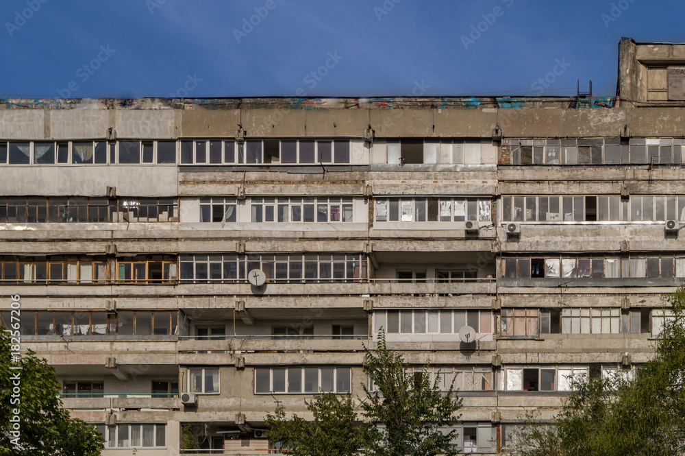 Old apartment house or dormitory with balconies, blue sky and green trees