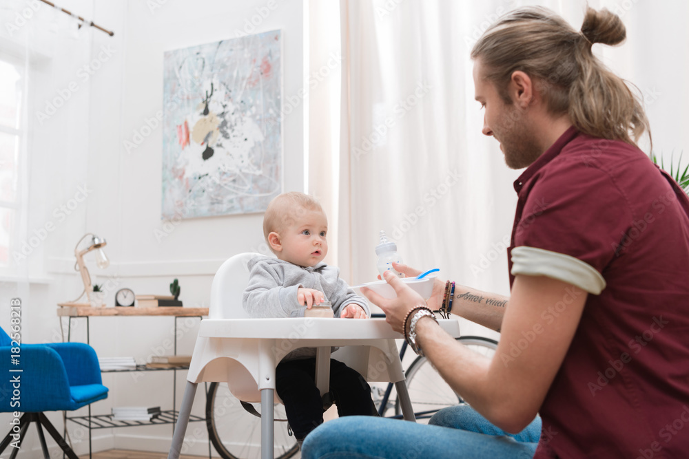 father feeding his little son with baby food at home father feeding his little son with baby food at home