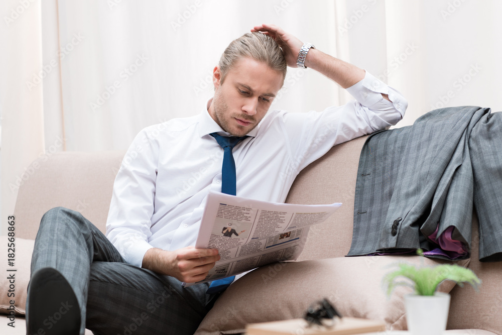concentrated businessman reading newspaper on sofa at home concentrated businessman reading newspaper on sofa at home