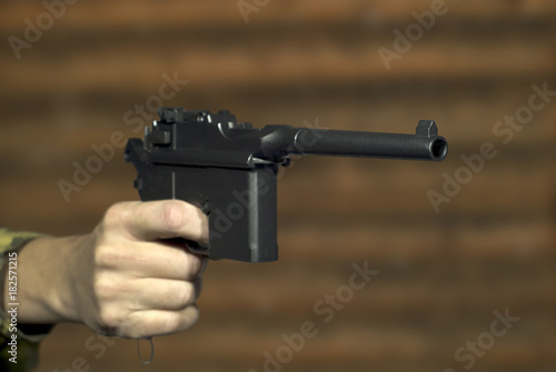 Принти на полотні A man's hand with a vintage semi-automatic pistol points past the frame on the background of a log wall