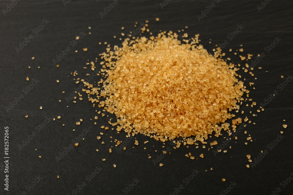Pinch of brown cane sugar spilled on black slate Pinch of brown cane sugar spilled on black slate