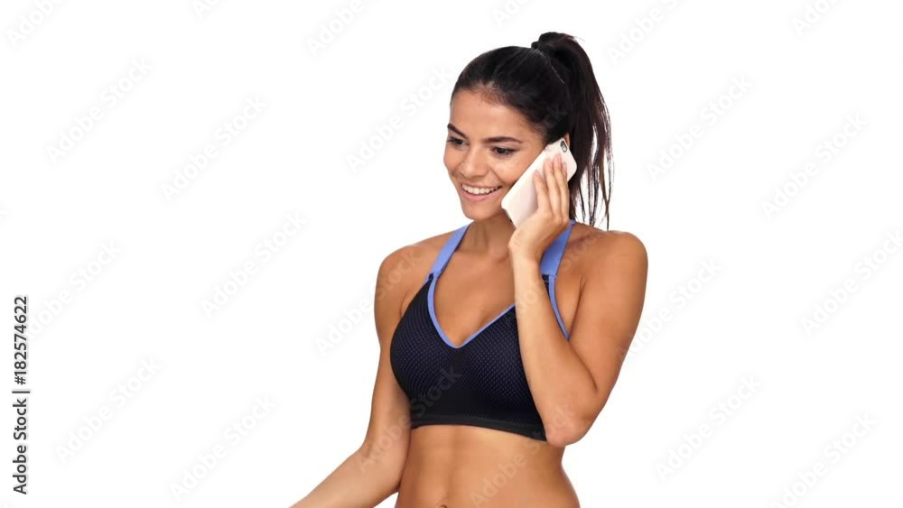 Smiling brunette sports woman doing exercise with dumbbells while talking by smartphone over white background Smiling brunette sports woman doing exercise with dumbbells while talking by smartphone over white background