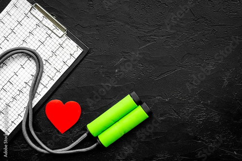 Prevent heart disease. Heart sign, cardiogram, jump rope on black background top view copyspace photo