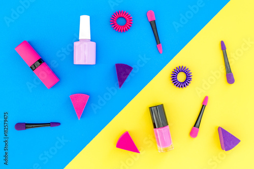 Bright decorative cosmetics. Pink and lilac nail polish and lipstick on blue and yellow background top view