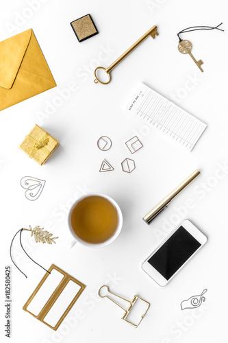 Office desk in trendy gold color. Glittering stationery near cup of tea, cell phone on white background top view